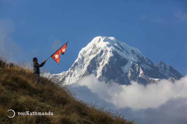 A happy trekker waves Nepali flag as Hiuchuli appears to float on clouds